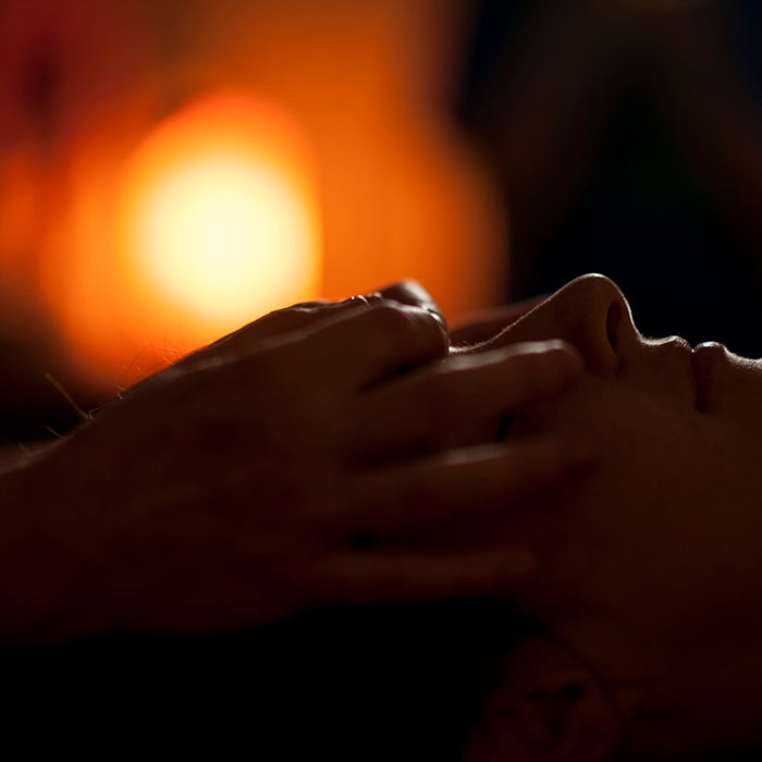 Hands massaging a person's face in a dimly lit room with warm bokeh