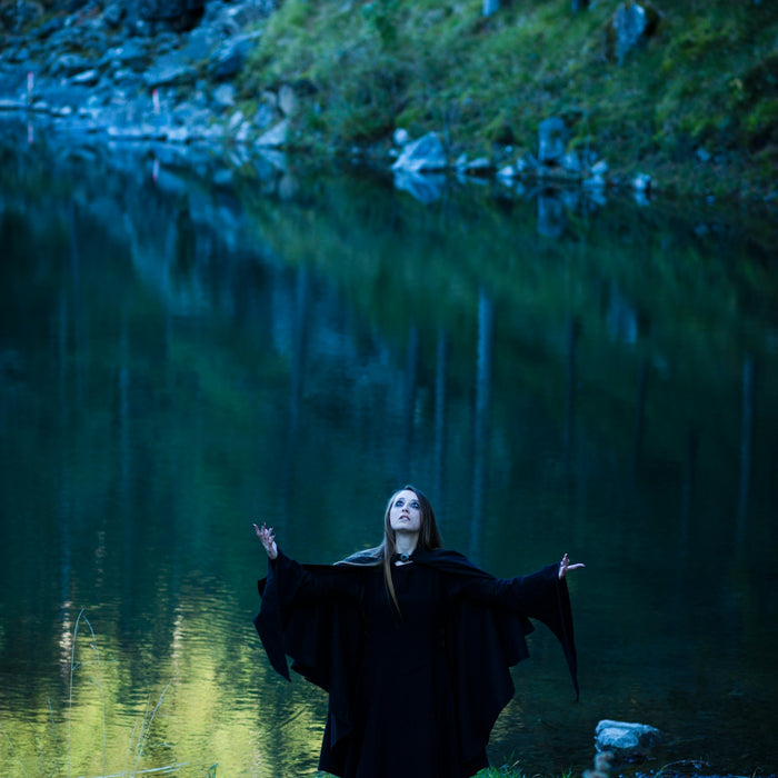 a woman dressed in black standing in front of a lake