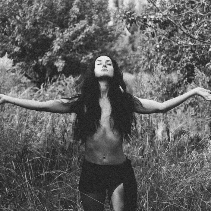 a person with long hair standing in a grassy area with the arms out
