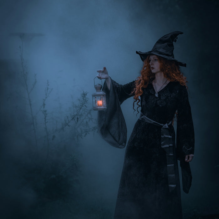 a woman dressed as a witch holding a lantern