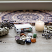 A chakra stone kit set on an altar with sage and lavender herbs and a candle