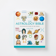 The Astrology Bible book by Judy Hall, featuring a white cover decorated with colorful astrological illustrations and zodiac symbols, shown against a light gray background.