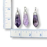 Three purple crystal pendants with silver settings on a ruler for scale.