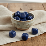 Ceramic bowl with blue stones on a wooden surface with a beige cloth