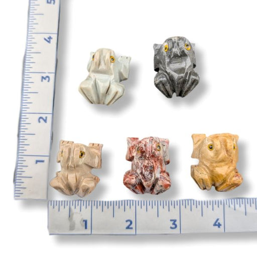 Five carved frog figurines in different stone colors and patterns, arranged on a white background with a ruler showing their dimensions.