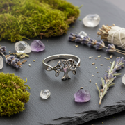 Silver tree-shaped ring on a dark surface with crystals and herbs