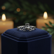 Silver ring with a heart design on a blue cushion in a dark setting with candles.