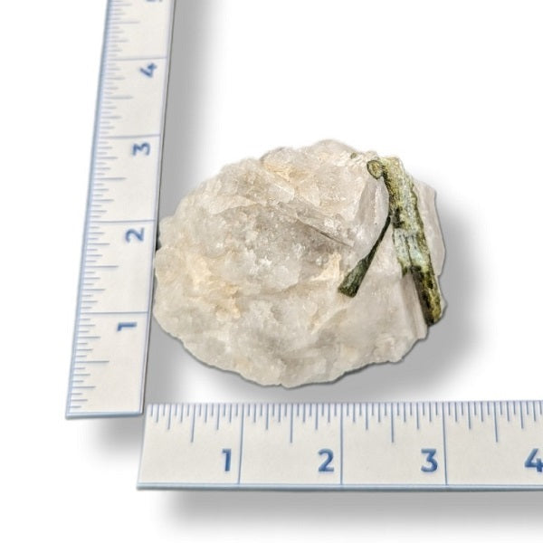 Rock with a green mineral on a white background with rulers for scale