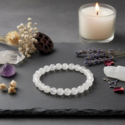 White beaded bracelet on a dark surface with a candle, crystals, and flowers.