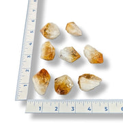Nine rough citrine crystals on a white background with a ruler for scale.