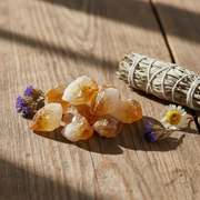 Crystal stones with flowers and a sage bundle on a wooden surface