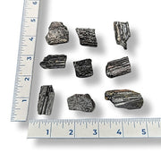 Black tourmaline rods with a ruler for scale on a white background