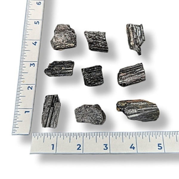Black tourmaline rods with a ruler for scale on a white background
