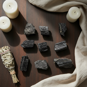 Black Tourmaline, candles, and a smudge stick on a wooden surface with beige fabric.