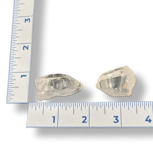 Two crystal-like rocks next to a ruler on a white background