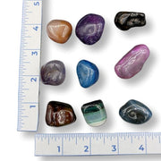 Multicoloured dyed agates tumbled on a white background with a ruler for scale.
