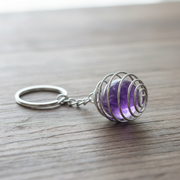 Silver Spiral Cage Keychain with purple gemstone on a wooden surface