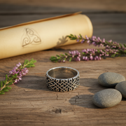Silver ring with intricate design on a wooden surface with stones and flowers