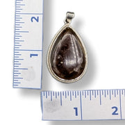 Teardrop-shaped pendant with brown stone on a white background with ruler for scale