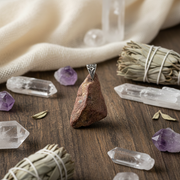 Pendant on a stone surrounded by crystals and smudge sticks on a wooden surface