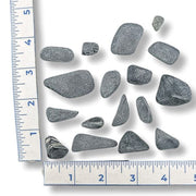 Black Jade Tumbled  of different sizes next to a ruler on a white background
