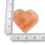 Heart-shaped orange selenite next to a ruler on a white background