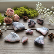 Rhodonite tumbled on a wooden table with roses and baby's breath