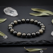 Black beaded bracelet on a dark surface with leaves and crystals