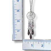 Necklace with a dreamcatcher pendant and beads next to a ruler for scale on a white background