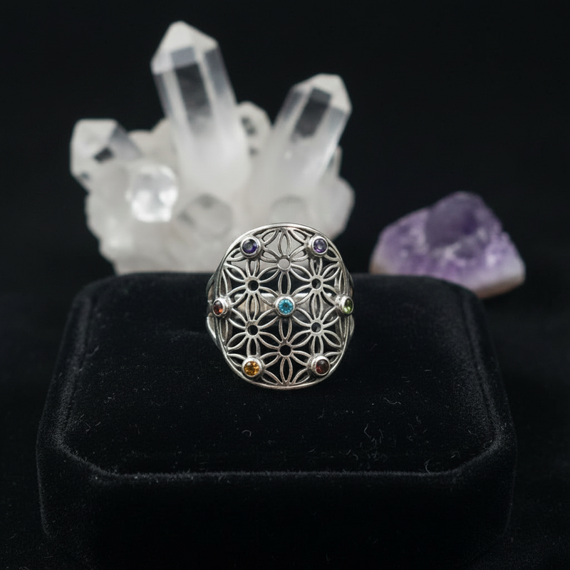 Silver ring with floral design and embedded gemstones on a black ring pillow with crystals in the background.