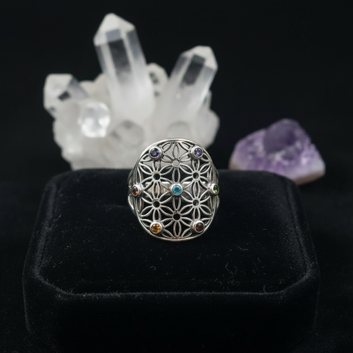 Silver ring with floral design and embedded gemstones on a black ring pillow with crystals in the background.