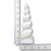 White spiral decorative selenite next to a ruler for scale on a white background