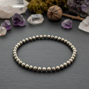 Silver beaded bracelet on a dark surface with crystals and plants in the background