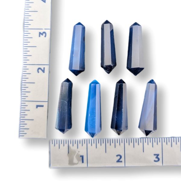 Six faceted blue crystal points arranged on a white background with ruler markings showing their dimensions.