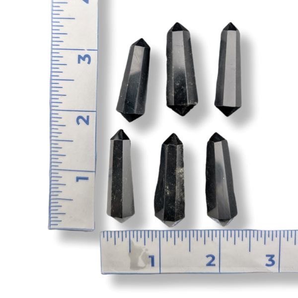 Six black crystal points arranged on a white background with two metal rulers on the left and bottom edges for size reference.