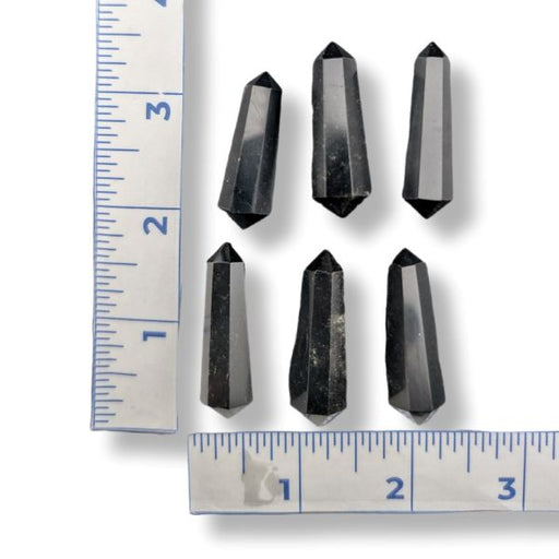 Six black crystal points arranged on a white background with two metal rulers on the left and bottom edges for size reference.