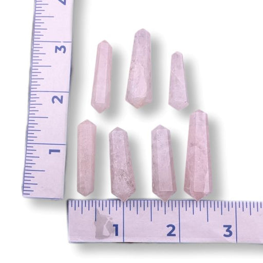 Seven pale pink crystal points arranged on a white background with ruler measurements along the left and bottom edges to show size.