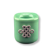 A mini green candle holder  with a silver-colored metal Celtic knot charm in the center, shown on a white background with a soft drop shadow.