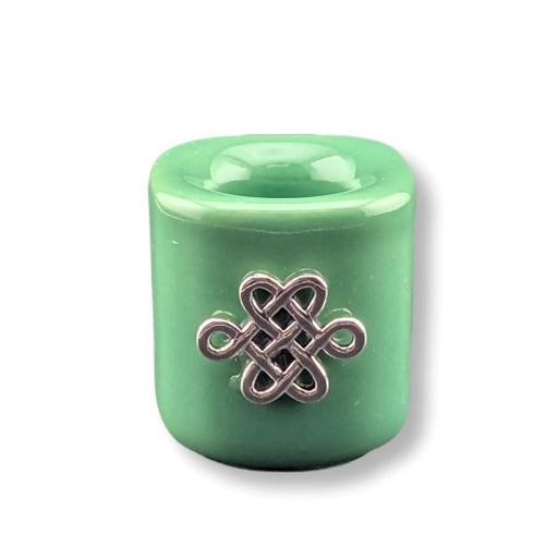 A mini green candle holder  with a silver-colored metal Celtic knot charm in the center, shown on a white background with a soft drop shadow.