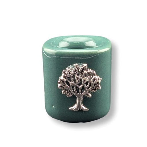 A mini ceramic green candle holder with a charm of a silver tree of life motif on the front, set against a plain white background.