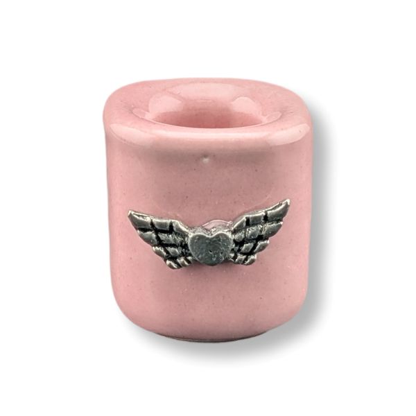 A light pink mini candle holder with a  charm featuring a silver-toned metal winged heart detail on the front, set against a plain white background.