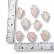 Seven raw, rough translucent stone rose quartz arrowheads arranged on a white background with a blue ruler on the left and bottom for size reference.