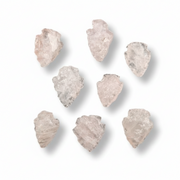 Seven raw, irregular pale pink quartz crystal arrowheads arranged on a clean white background with soft drop shadows.