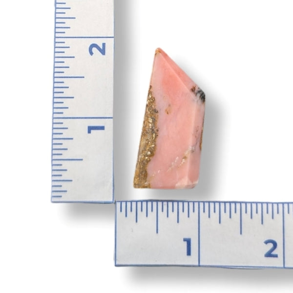 Pink stone with gold specks next to a ruler on a white background