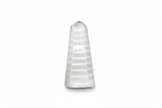 Selenite obelisk with horizontal striations, photographed against a seamless white background.