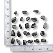 Collection of black stones with a ruler for scale on a white background