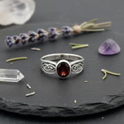 Silver ring with a red gemstone on a dark surface with lavender and crystals