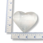 Heart-shaped selenite next to a ruler on a white background