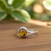 Silver ring with a yellow gemstone on a wooden surface with green leaves in the background