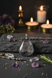 Crystal pendant on a dark surface with candles and herbs in the background